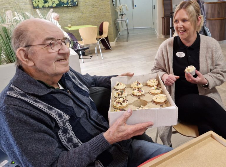 Elderly person holding a box of cupcakes